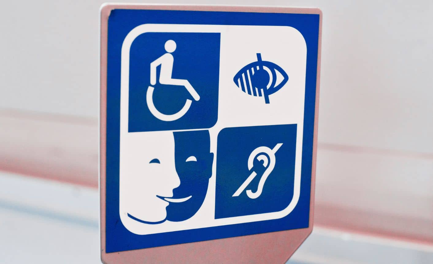 White-blue sign that features four accessibility symbols: a wheelchair symbol, a visual impairment symbol, the S3A pictogram and a hearing loop symbol.