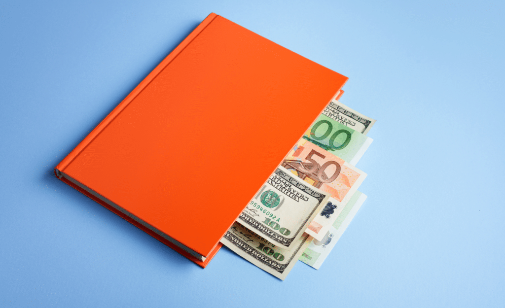 An orange book on a blue background with various paper currencies, including dollars and euros, peeking out from its pages.