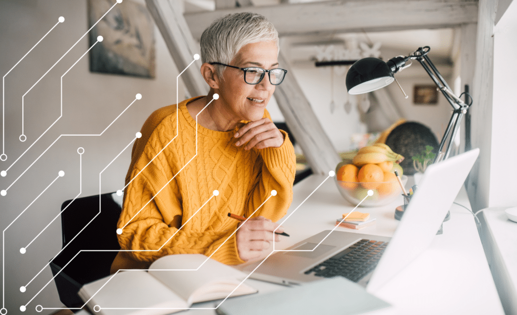 The best AI writing tools blog image is an older woman with grey hair and yellow jumper sitting in front of a laptop with pen in hand, with abstract lines representing AI input from the bottom left side of the screen.