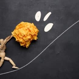 A wooden person moving a light-weight paper ball up a hill, symbolizing technical documentation software that makes work easier.